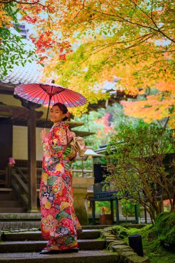 Geleneksel kimono tarzı retro şemsiyeli kadın, sonbaharda köyün bahçesinin ortasında tek başına duruyor, Japonya 'ya geliyor spor müsabakalarında seyahat ediyor ve ziyaret ediyor.