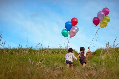 Bir grup mutlu küçük kız ellerinde renkli balonlar tutuyorlar. Yeşil bir çayırda oynayan bir çocuk. Gülümseyen çocuk, güzel gökyüzü gün batımı ve kuş sürüsü