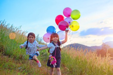 Bir grup mutlu küçük kız ellerinde renkli balonlar tutuyorlar. Yeşil bir çayırda oynayan bir çocuk. Gülümseyen çocuk, güzel gökyüzü günbatımı...