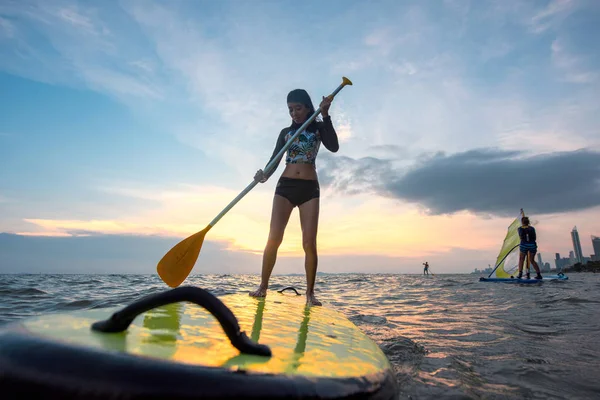 年轻苗条身材的女子的侧影 试图用划桨的方式玩冲浪板 并期待着在大海中央冲浪 — 图库照片