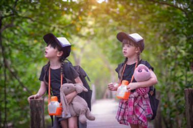 Orman ormanının tahta köprüsünde yürüyen ikiz çocuklar doğa eğitimini yenilemek için saha gezisine katılacaklar.  