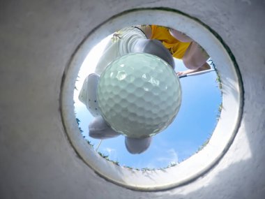 view of bottom low angle of the golf hole, a golf ball in hand of golf player being takes away from the hole on the green by woman golf player after putted successfully a winner 