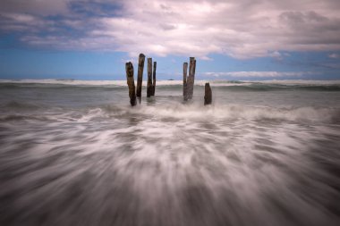 Güneşli bir günde, eski bir tahta direğin manzarası deniz kıyısında uzun süre bekleyen bir felaket, deniz dalgasının kumsala çarpması gibi.