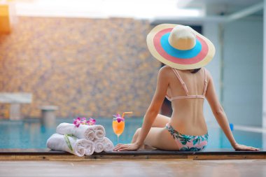 Bir bardak portakal suyuyla yüzme havuzunun kenarında oturan sıska genç kadın, yaz tatilinde ve tatilde rahat bir hayat yaşa.