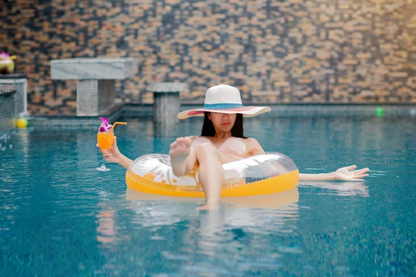 woman sitting in swimming tube floating in pool,  enjoy and relax happiness emotion with glass of orange juice holding in hand, for life comfortable, exercise swimming