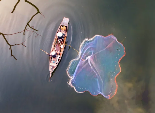 top view, aerial view, bird eyes view of fisher man on old wooden boat fishing by throwing fishing net to river during sunset in rural of Thailand