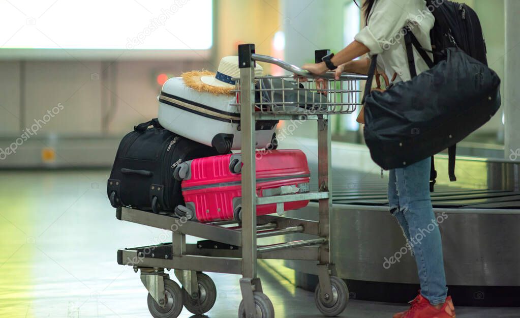 many suitcases and luggages in airport cart after taken from transfer belt of the airport terminal, being push or tow by hand of woman traveler to keep away in arrival hall of the airport, traveling to destination concep