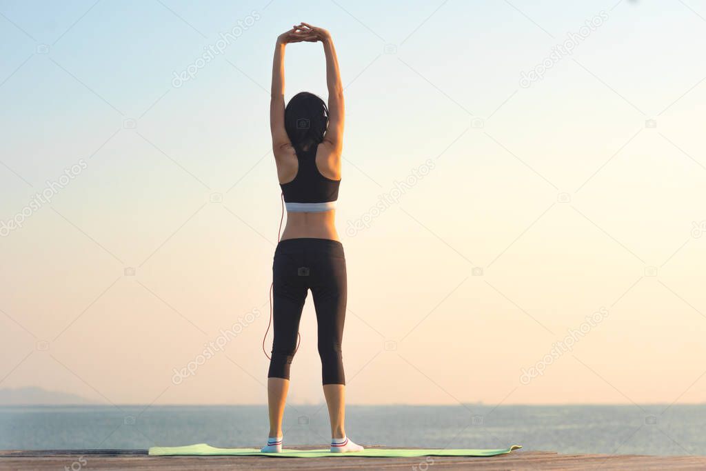 sport woman in practice of exercise on wooden bridge at sunset, enjoy music while workout on the pier jetty in the se