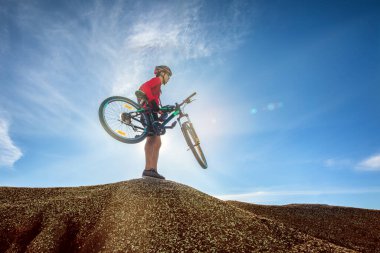 Bisikletçi kollarında bisikletini taşırken mavi gökyüzü arka planında yürüyordu. Sağlıklı konsept için aktif açık hava yaşam tarzı.