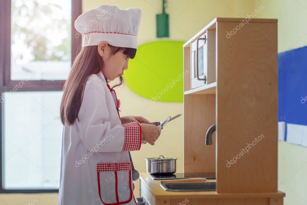 little girl pretending in chef cooking in classroom, one of the subject teaching kids in school for future occupation favorite