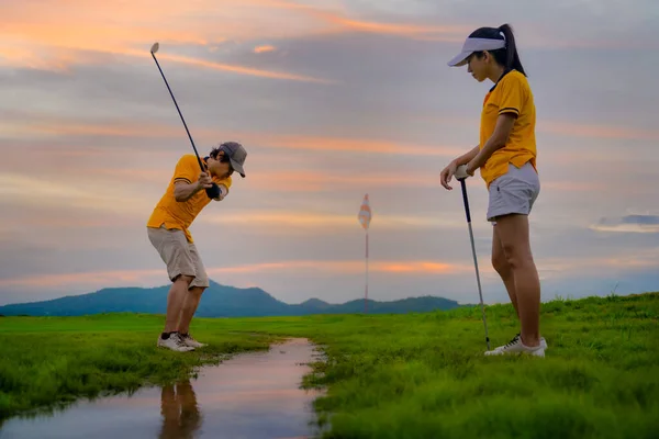 golf ball dropped in water in channel raceway of the golf course, going to hit away to destination on the green by golf player, along with golf-mate or competitor in an exciting beside in background