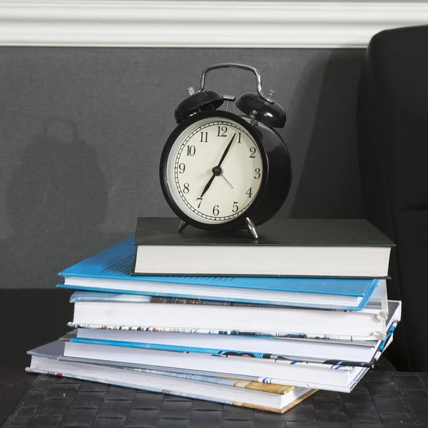 Black alarm clock on a black and white striped napkin showing 7 o'clock on a bedside table — Stock Photo, Image
