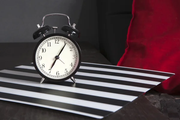 Relógio de alarme preto em um guardanapo listrado preto e branco mostrando 7 horas em uma mesa de cabeceira — Fotografia de Stock