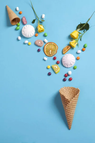 Marshmallows, doces, geléias, doces e canecas secas laranjas caindo em cone wafer sobre fundo azul — Fotografia de Stock