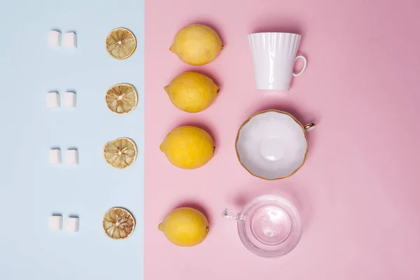 O conjunto de chá. Açúcar refinado, limão, laranja, xícaras e colheres como ornamento em papel rosa e azul — Fotografia de Stock