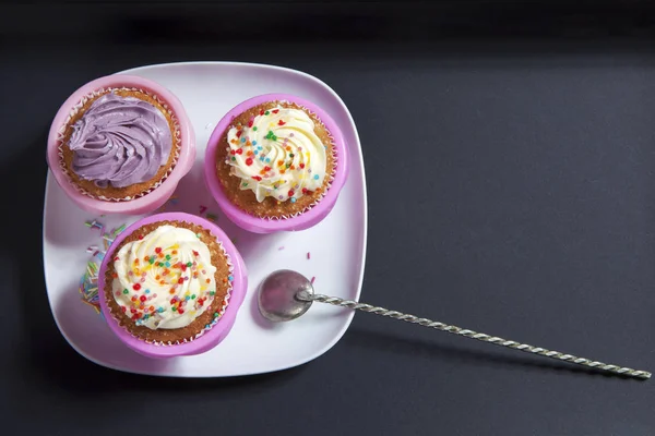 Los cupcakes con crema blanca y violeta con cucharas sobre el fondo negro —  Fotos de Stock