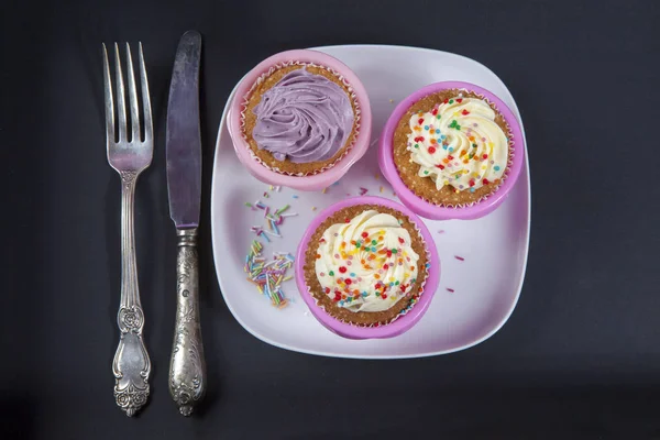Os cupcakes com creme branco e violeta com garfo e faca no fundo preto , — Fotografia de Stock