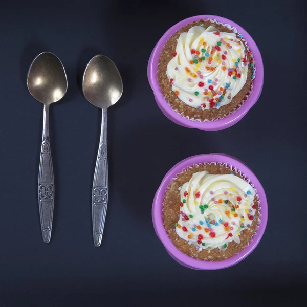 The cupcakes with white and violet cream with spoons on the black background — Stock Photo, Image