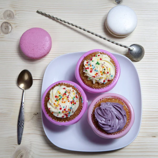 Os cupcakes com creme branco e violeta com colheres no fundo de madeira , — Fotografia de Stock