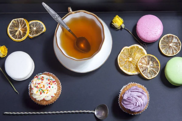 Té en una taza y platillo, rosas amarillas secas, pastel sobre un fondo negro . —  Fotos de Stock