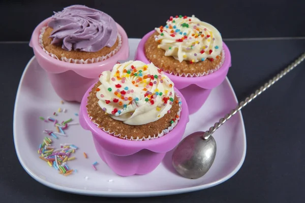 Os cupcakes com creme branco e violeta com colheres no fundo preto — Fotografia de Stock