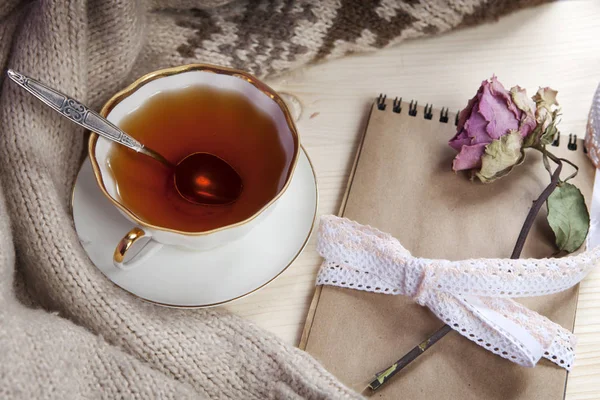Винтажная чашка чая, завернутая в шерстяную клетку и блокнот с сухой розой на столе — стоковое фото