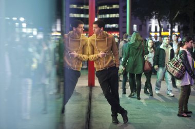 Bir adam ayakta, cam duvara yaslanmış bir sarı kazaklı M ve M Piccadilly Circus üzerinde depolamak. Kulaklıklar müzik dinlediği.