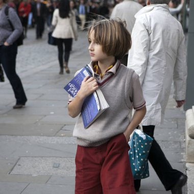 Onun göğsüne kitap basarak sokakta, on yıl içinde bordo şort ve bej yelek şık bir çocuk duruyor