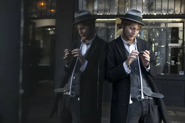Street actor magician in a hat and a strict suit is leaning against a mirror display. — Stock Photo, Image