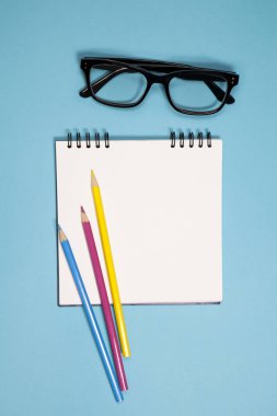 Yaylar, gözlük ve renkli kalemler mavi bir arka plan üzerinde beyaz dizüstü bilgisayar.