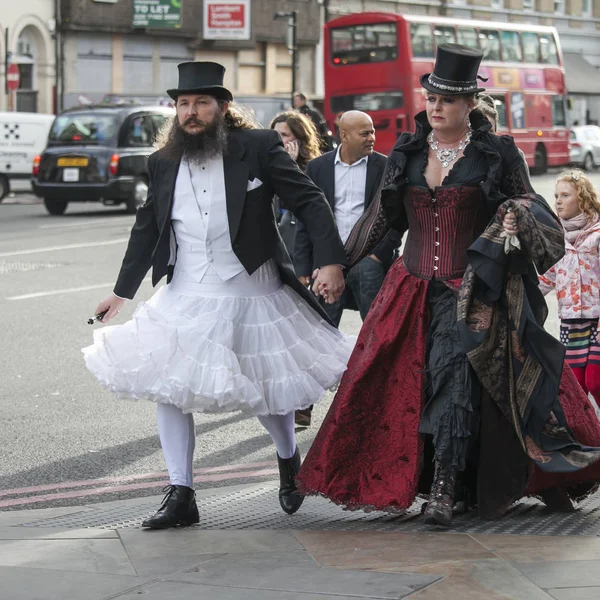 A man in a white wedding dress and a top hat with a woman in a gothic red velvet dress walking down the street in London Bridge — Stock Photo, Image