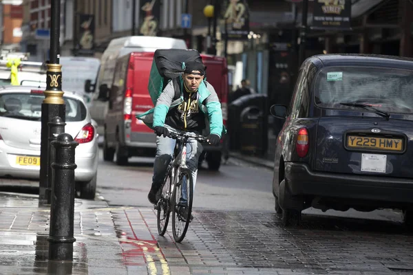 Велосипедист в серо-зеленой куртке и с сумкой "Доставка" мчится между машинами по дороге . — стоковое фото