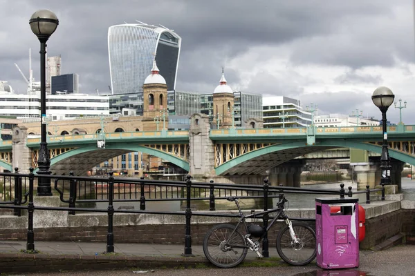 O bicicletă este lângă un coș de gunoi roz în apropierea digului de pe fundalul orașului Londra. — Fotografie, imagine de stoc