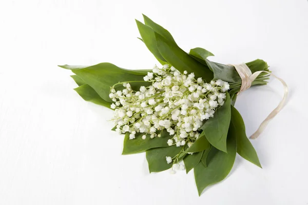 A bouquet of lilies of the valley bandaged with a pink ribbon on a white wooden table — Stock Photo, Image