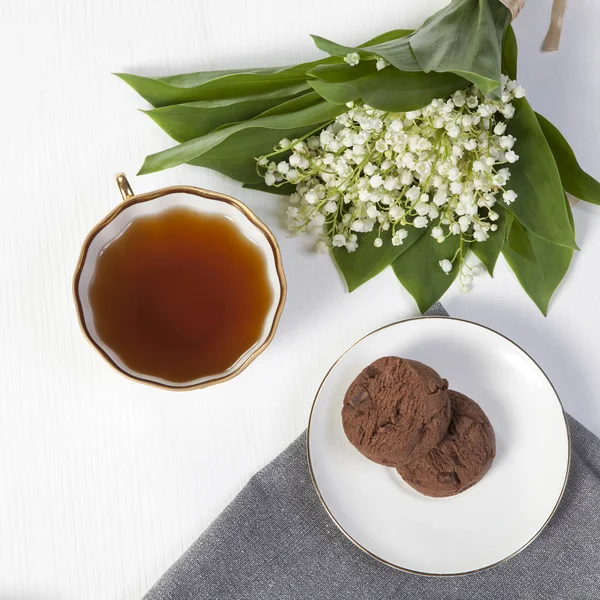 White cup of coffee, a bouquet of lilies of the valley, a notepad for notes and a saucer with two brownie cookies. Breakfast. Copy space — Stock Photo, Image