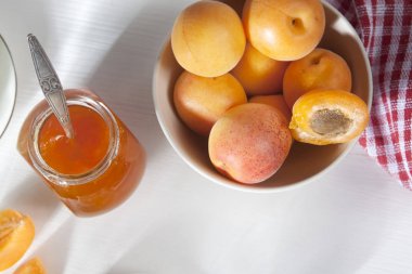 bir kase ve bir kırmızı ve beyaz havlu, el yapımı yaz boşlukları ile beyaz bir tabloda bir kavanoz reçel kayısı