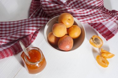 bir kase ve bir kırmızı ve beyaz havlu, el yapımı yaz boşlukları ile beyaz bir tabloda bir kavanoz reçel kayısı