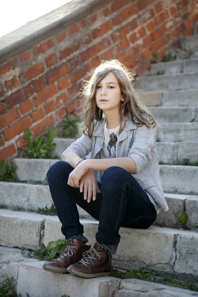 Грустная девушка с длинными волосами в джинсах тринадцати лет сидит на ступеньках — стоковое фото
