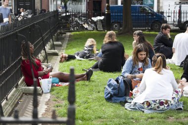 Office katip çimlere oturup ve yüzleri güneşe maruz altın meydanında, Soho, yemek