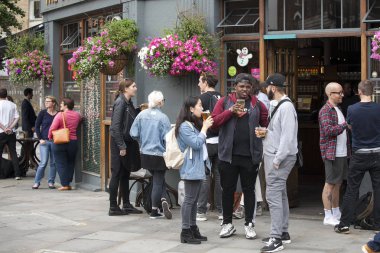 Rengarenk kalabalık pub dışında oturur, bira içiyor, arkadaşlarıyla konuşuyor. Semt pazarı