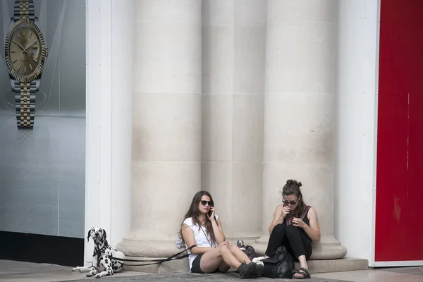 Δύο κορίτσια στο σορτς κάθονται, κλίνει ενάντια στους πυλώνες κοντά το θέατρο στο Κόβεντ Γκάρντεν. Το σκυλί Δαλματίας κάθεται δίπλα τους — Φωτογραφία Αρχείου