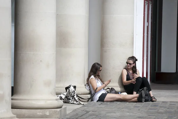Twee meisjes in korte broek zitten, leunend tegen de pijlers in de buurt van het theater in Covent Garden. De Dalmatische hond zit ernaast — Stockfoto