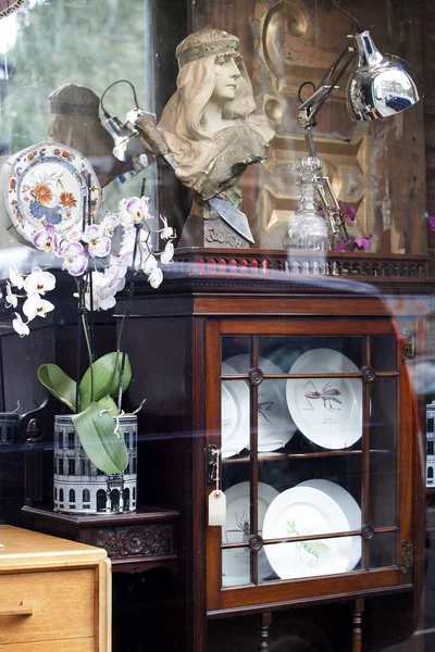 Showcase of an antique store with a sculpture, orchids in a vase and plates in a closed cupboard — Stock Photo, Image