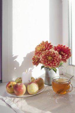 Teneke bir kavanoz, kabak, bir fincan çay ve güneşli havalarda penceresinde üzerinde elma kırmızı dahlias ile sonbahar natürmort