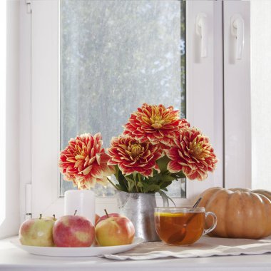 Teneke bir kavanoz, kabak, bir fincan çay ve güneşli havalarda penceresinde üzerinde elma kırmızı dahlias ile sonbahar natürmort