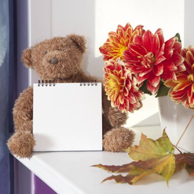 sonbahar dahlias buket yanında oyuncak ayı. Oyuncak ayı yazmak için bir not defteri tutar.
