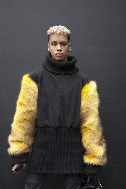 Sarı el ile yapay kürk yapılan bir Siyah kazaklı genç adam dar siyah pantolon ve topuklu tarçın çizmeler