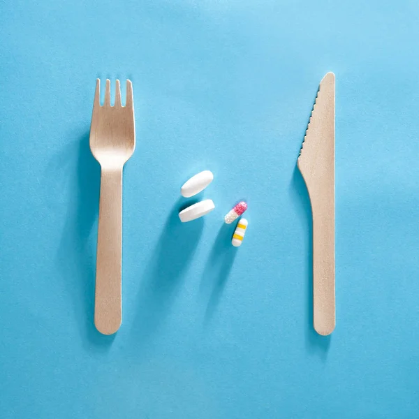 El tenedor con el cuchillo y las pastillas entre sobre el fondo azul . — Foto de Stock