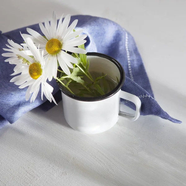 Margaritas en una taza de esmalte blanco y una servilleta azul sobre una mesa de madera blanca —  Fotos de Stock