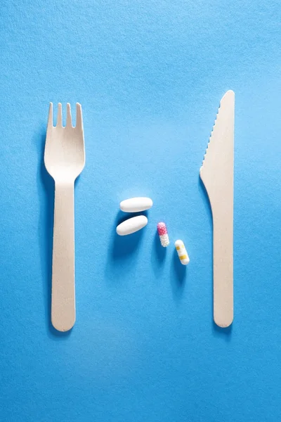 El tenedor con el cuchillo y las pastillas entre sobre el fondo azul . —  Fotos de Stock